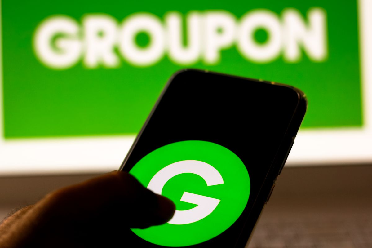 A man holding his phone with the Groupon logo