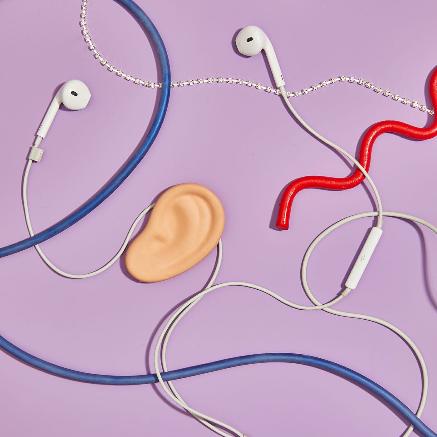 White earbuds, some wires, and fake ear on a purple background